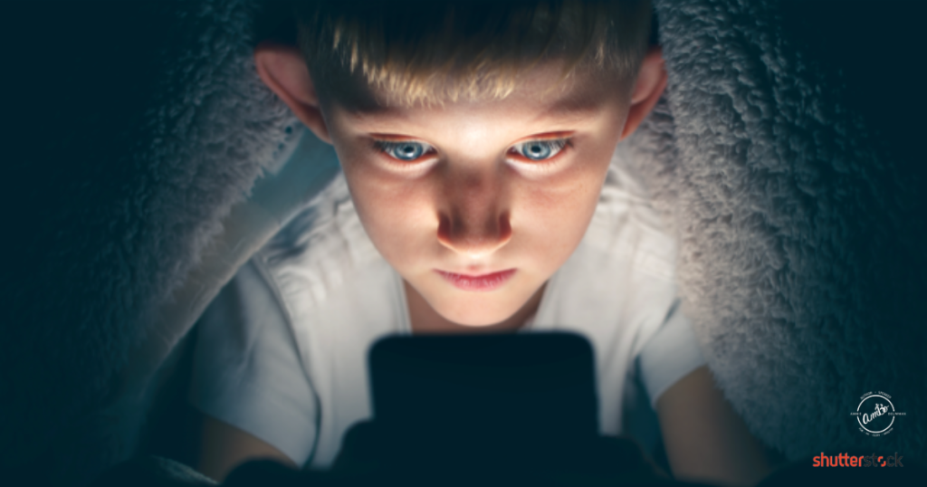 A boy looking at the camera with his phone.