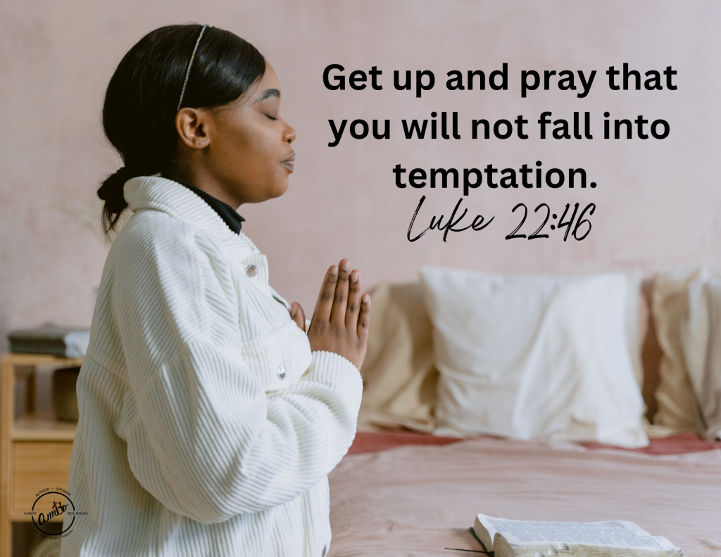 A woman is praying in front of the bed.