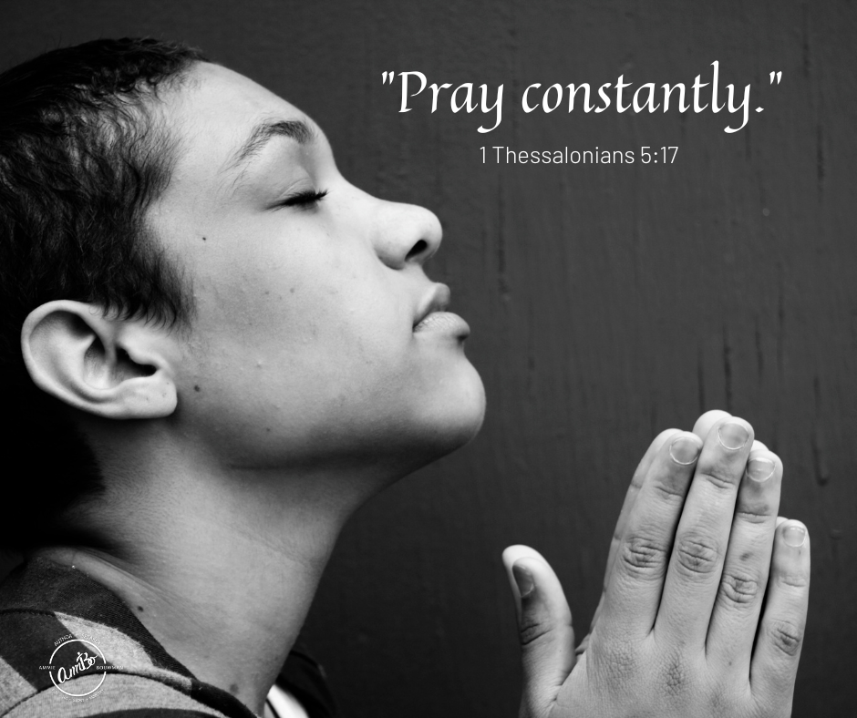 A young boy is praying with his hands in the air.