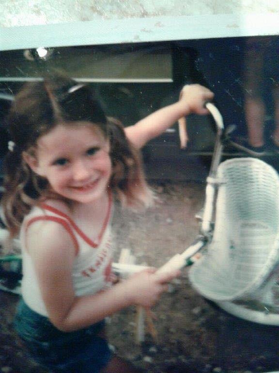 A young girl is holding a hose and smiling.